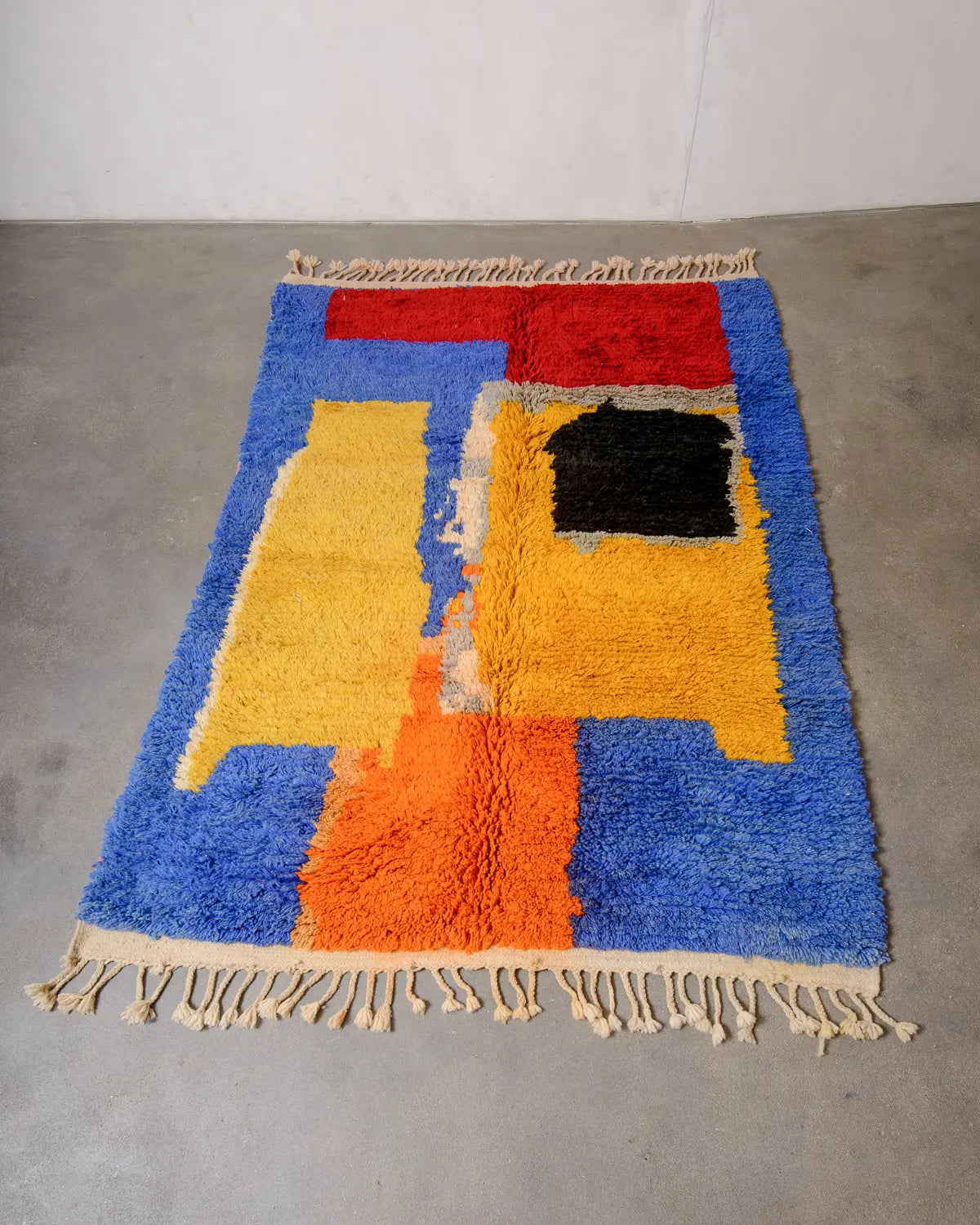 Vintage wool Berber rug made of bright colours laying flat on concrete studio floor.